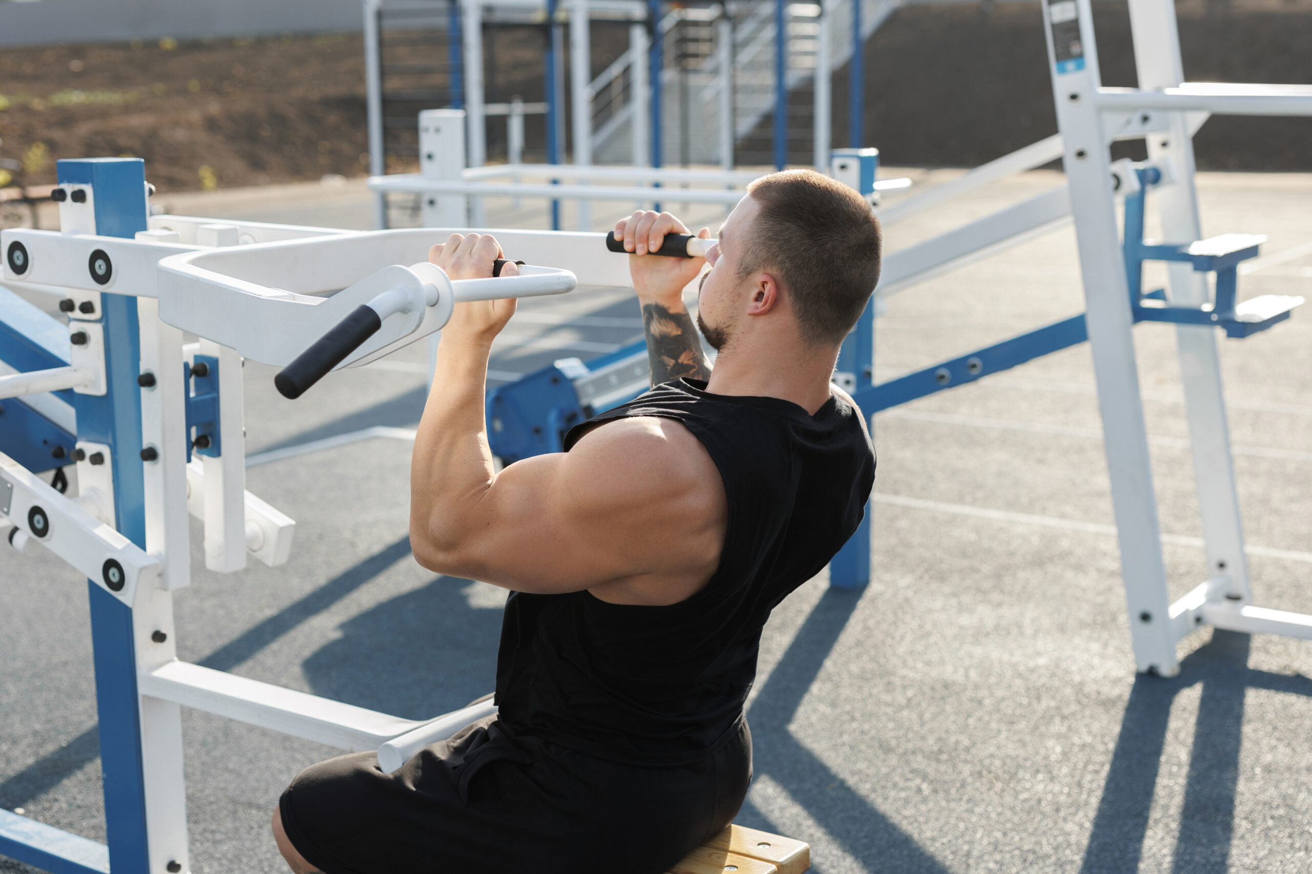 A sexy young muscular man does an exercise for the upper chest on an open-air simulator.